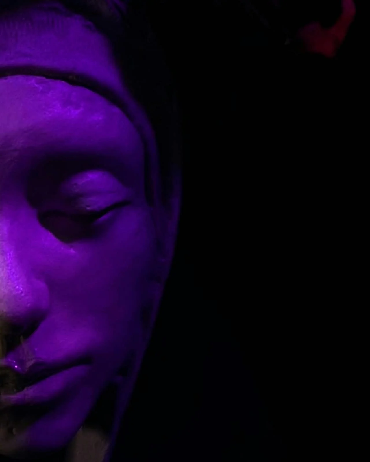Rostro de una escultura de mujer iluminado con luz violeta