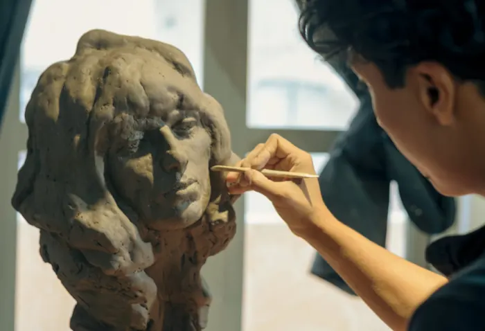 Un escultor del taller afina con una herramienta el rostro de un busto de arcilla