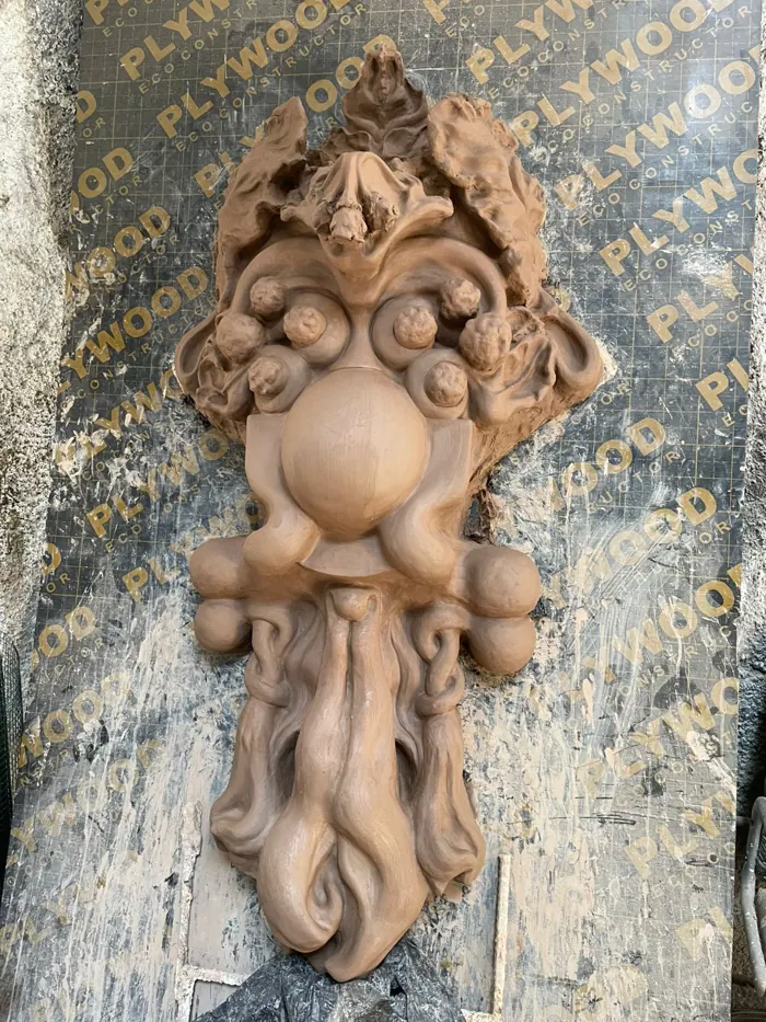 Mascarón ornamental con rostro y volutas, en arcilla