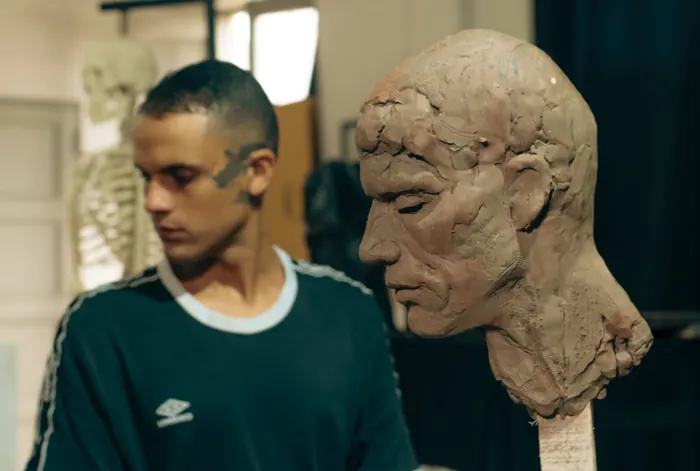 Un integrante del taller junto a una cabeza de arcilla